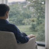 窓の外を見つめながら静かに考え込む40代男性、医療脱毛を申し込む直前の迷いの時間