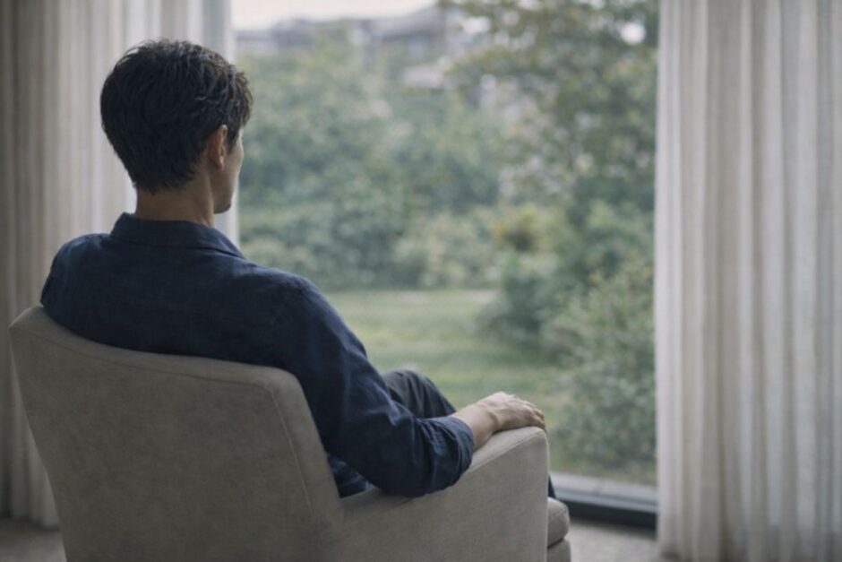 窓の外を見つめながら静かに考え込む40代男性、医療脱毛を申し込む直前の迷いの時間