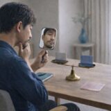 天秤の前で手鏡を使い、ヒゲの白髪を確認する40代男性の様子